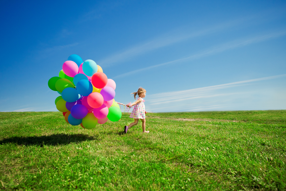 Little girl holding colorful balloons. Child playing on a green